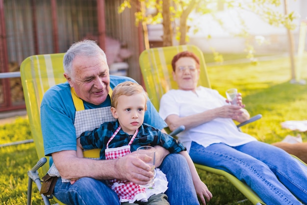 Les grands-parents s'amusent avec leur petit-fils, assis dans leur jardin et souriant.
