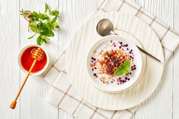 Granola d'avoine avec framboises séchées, myrtilles et noix avec du lait et garni de miel dans un bol blanc sur une table en bois, vue paysage d'en haut, gros plan, mise à plat