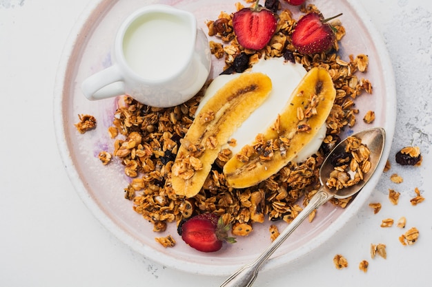 Granola d'avoine avec yaourt, fraises fraîches et banane, graines de chia, tournesol et miel dans une assiette en céramique blanche sur une surface claire