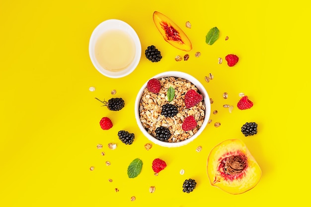 Granola croquant, baies et menthe dans un bol en céramique et framboises, mûres, pêche et miel.