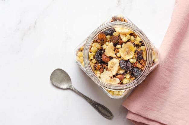 Granola fait maison avec des tranches de banane séchées aux noix et des canneberges séchées dans un bocal en verre avec une cuillère