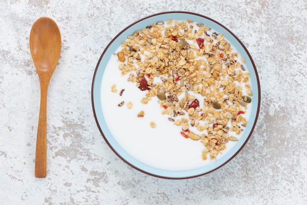 Photo granola, flocons d'avoine avec du lait, du miel et des fraises sur une table en bois bleue.