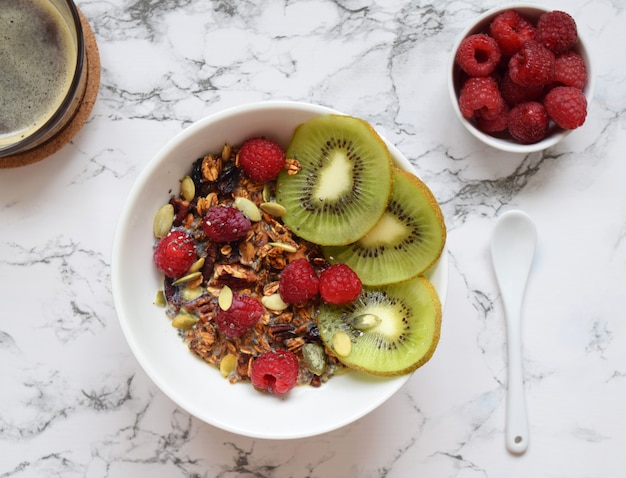 Granola maison avec chia, kiwi et framboises sur marbre blanc