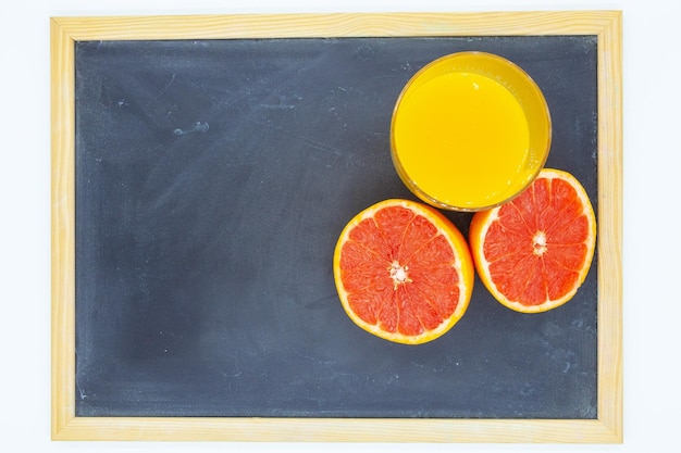 Photo grapefruit ou orange avec un verre de jus d'orange sur un tableau clair