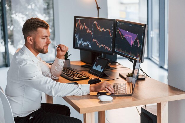 Graphiques et diagrammes Jeune homme d'affaires en vêtements formels est au bureau avec plusieurs écrans