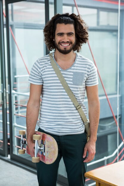 Photo graphiste souriant avec skateboard debout dans le bureau créatif