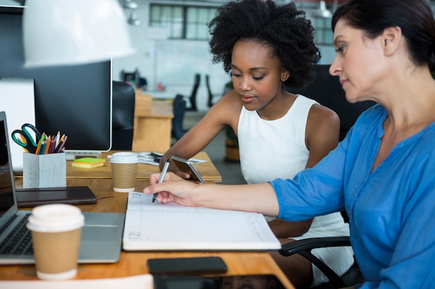 Photo graphistes féminins utilisant un téléphone mobile et prenant des notes