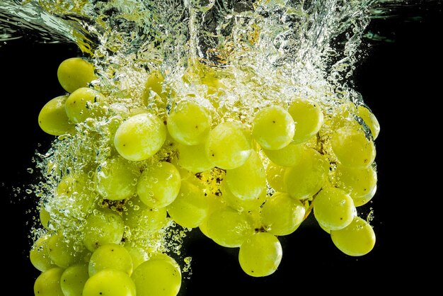 Une grappe de raisins blancs éclaboussée dans l'eau claire isolée contre un fond noir Photographie d'éclaboussure alimentaire