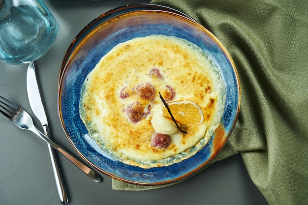 Gratin de baies avec de la glace dans un bol bleu sur une table en bois. Dessert au four français savoureux et sucré. Vue de dessus, mise à plat, composition centrale