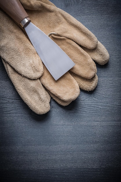 Grattoir à peinture en acier sur gants de travail et planche de bois