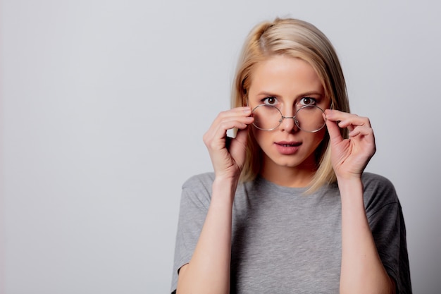 Grave femme blonde à lunettes sur mur blanc