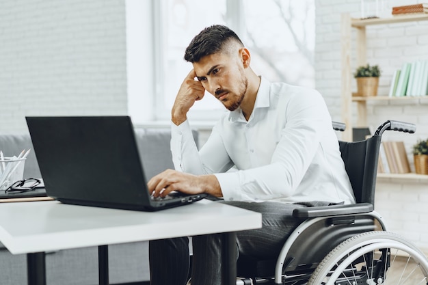 Grave handicapé concentré en fauteuil roulant à l'aide de son ordinateur portable pour travailler à la recherche d'un emploi sur internet