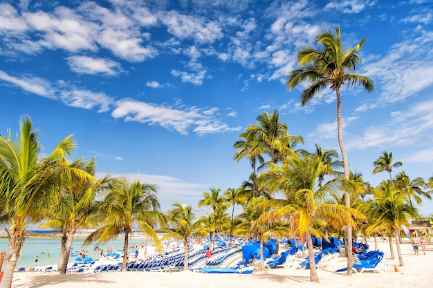 Great Stirrup Cay, Bahamas - 8 janvier 2016 : palmiers verts sur la plage de sable blanc avec chaises longues, personnes et mer turquoise ou océan par beau temps sur ciel bleu. Vacances d'été, station balnéaire. paradis