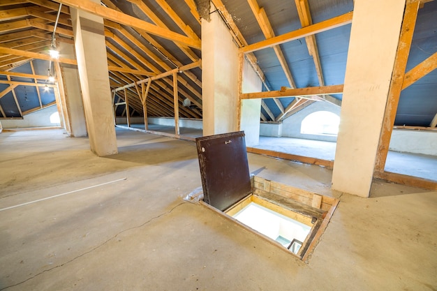 Grenier d'un bâtiment avec des poutres en bois d'une structure de toit et une porte de secours en étage.