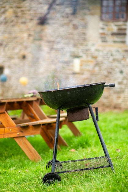 Un gril rond fumant sur fond de tables en bois avec bancs Se préparant pour un pique-nique en plein air