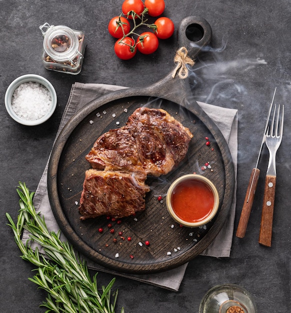 Grill de steak de boeuf barbecue avec sauce fumée tomates sel et romarin sur planche de bois noir sur fond sombre