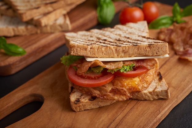 Grillé et sandwich avec bacon, œuf frit, tomate et laitue servi sur une planche à découper en bois