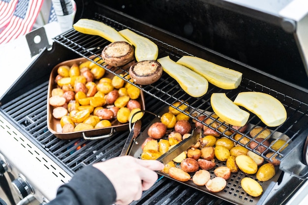 Griller de petites pommes de terre avec des tranches d'ail sur un gril à gaz extérieur.