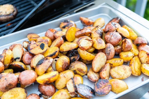 Griller de petites pommes de terre avec des tranches d'ail sur un gril à gaz extérieur.