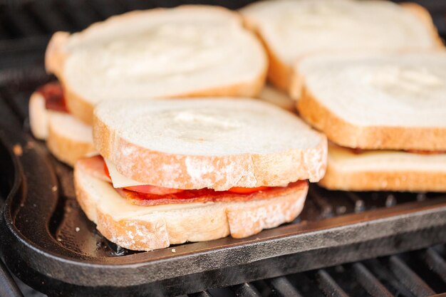 Griller un sandwich au fromage grillé avec des lanières de bacon et des tomates fraîches sur un gril à gaz extérieur.