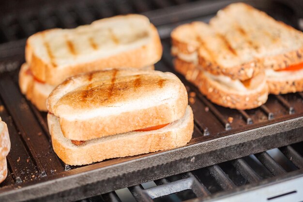Griller un sandwich au fromage grillé avec des lanières de bacon et des tomates fraîches sur un gril à gaz extérieur.