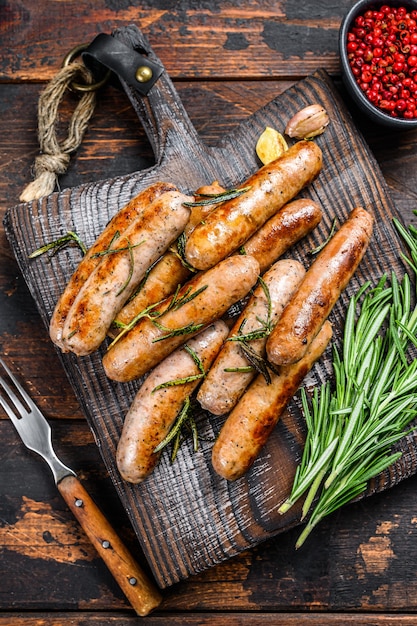 Griller des saucisses bavaroises sur une planche à découper. Fond en bois foncé. Vue de dessus.