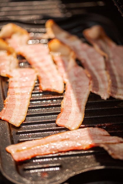 Griller des tranches de bacon sur une plaque chauffante en fonte dans un gril à gaz extérieur.