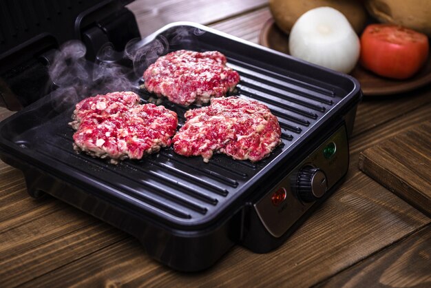 Griller la viande pour les hamburgers dans un gril électrique sur une table en bois