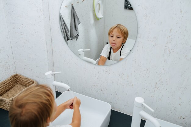 Photo grimaçant dans un miroir petit garçon se lavant les mains dans le lavabo de la salle de bain