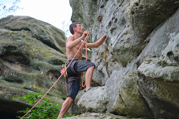 Grimpeur déterminé escaladant le mur escarpé d'une montagne rocheuse Sportif surmontant une route difficile S'engageant dans des sports extrêmes et un concept de passe-temps d'escalade