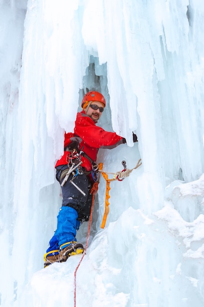 Grimpeur sur glace sur un mur vertical d'une cascade gelée parmi d'énormes glaçons