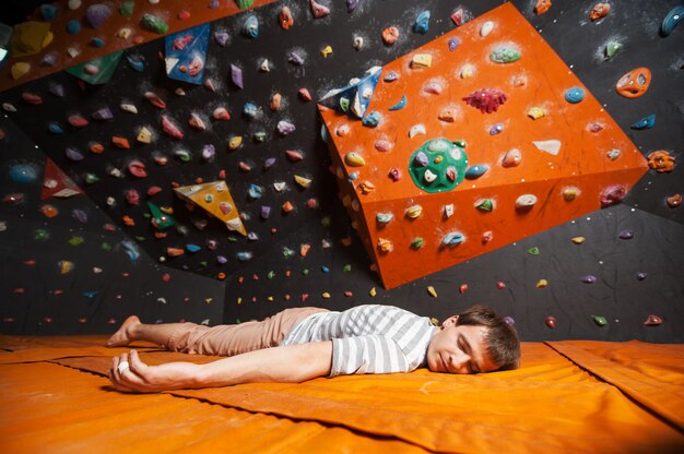 Grimpeur mâle fatigué sur le tapis près de la paroi rocheuse