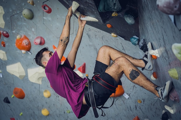 Un grimpeur mâle fort escalade un mur artificiel avec des poignées et des cordes colorées