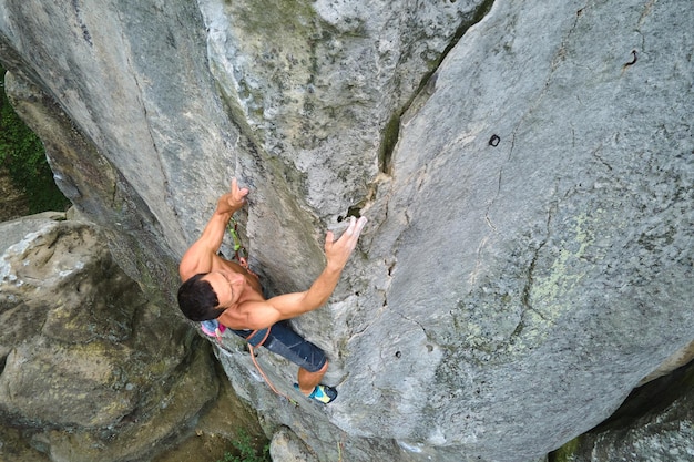 Grimpeur masculin fort escaladant le mur escarpé de la montagne rocheuse. Sportif surmontant la route difficile. S'engager dans le concept de passe-temps de sports extrêmes.