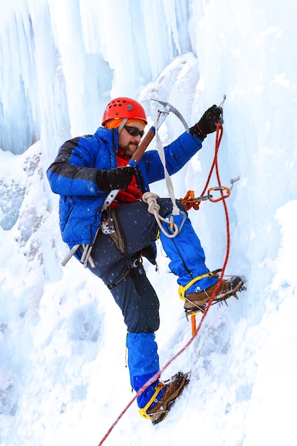 Le grimpeur avec le piolet prend d'assaut la paroi verticale du glacier