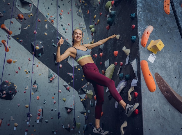 Une grimpeuse forte escalade un mur artificiel avec des poignées et des cordes colorées