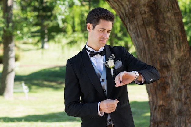 Groom attrayant vérifiant le temps dans le jardin