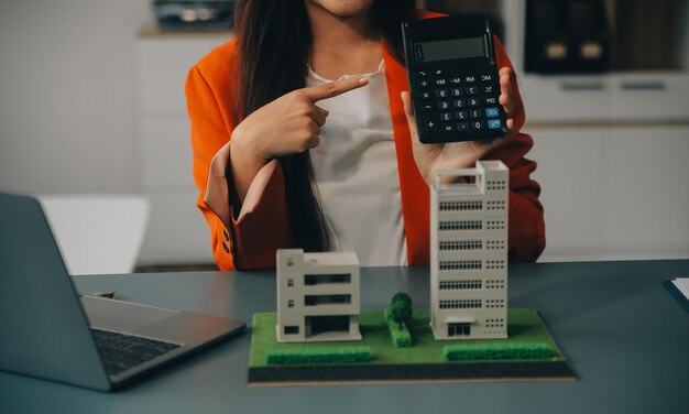 Photo en gros, l'agent immobilier s'assoit à la table, tient une petite maison, un modèle de cottage, un achat d'immobilier, une nouvelle propriété, une société de construction, fait une offre spéciale au client, un concept de logement abordable.