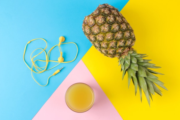 Un gros ananas et jus de fruits mûrs sur une table jaune vif, bleu et rose. l'été. vue d'en-haut.