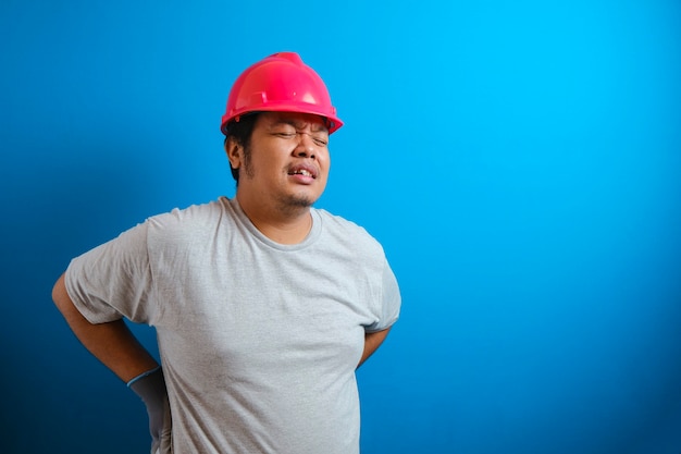 Un gros asiatique portant un casque rouge ressent une douleur dans le dos. L'homme se tient le dos tout en endurant la douleur