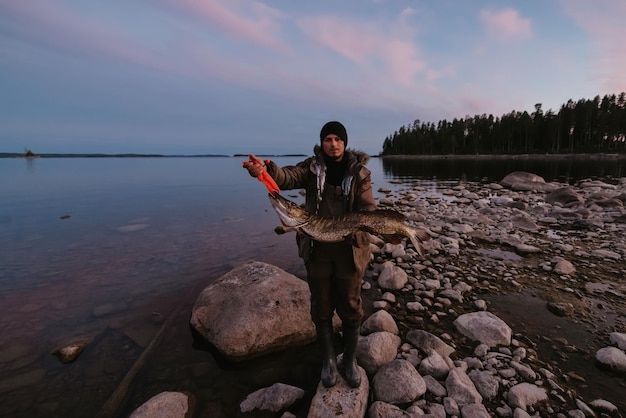 Gros brochet pêché dans les mains d'un pêcheur masculin sur la rive du lac