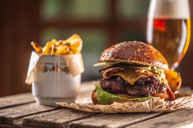 Gros Burger Avec Boeuf, Fromage, Oignon Caramélisé, Laitue, Tomate, Cornichon, Le Tout Dans Un Petit Pain à Côté De Quartiers De Pommes De Terre Et D'un Verre De Bière Pression.