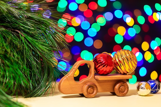 Gros camion jouet en bois a apporté des boules de Noël colorées à un arbre de Noël sur fond de nombreuses lumières colorées Photo pour la carte de voeux design du Nouvel An