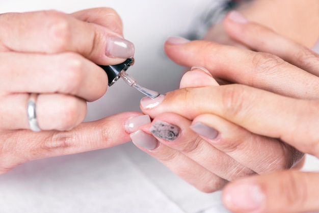 Gros coup d'une esthéticienne appliquant du vernis à ongles à un ongle féminin au salon de manucure.