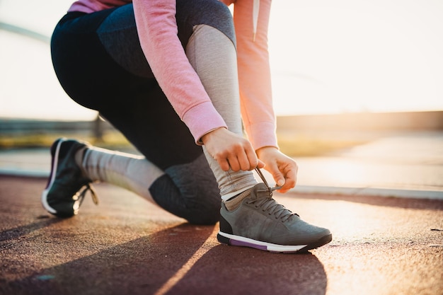 Gros coup de jogger féminin attache des chaussures sur des baskets. Beau pont de rivière et coucher de soleil en arrière-plan.