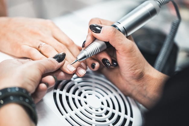 Gros coup de manucure de matériel dans un salon de beauté. La manucure applique une lime à ongles électrique à la manucure des doigts féminins.