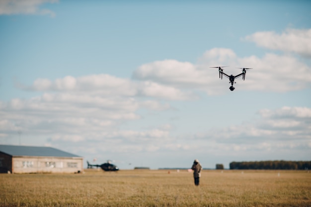 Gros drone quadricoptère en vol aérien et filmant un homme et un hélicoptère.