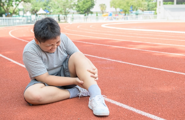 Gros garçon asiatique tenant sa blessure à la jambe de sport. muscle douloureux