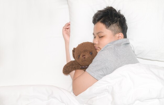 Un gros garçon obèse dort avec un ours en peluche dans son lit à la maison, un doux rêve et un concept de repos