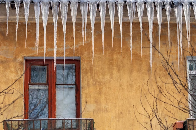 De gros glaçons pendent du toit d'une vieille maison Danger de chute de glaçons